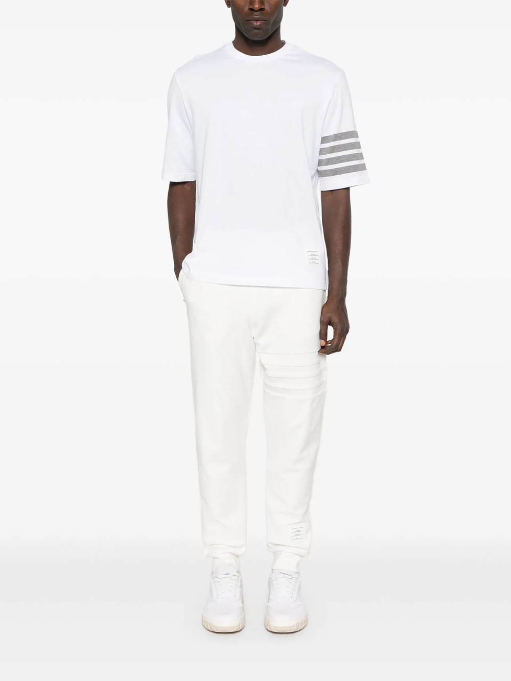 Thom Browne white cotton jersey short sleeve tee with four grey-bar stripe detail on sleeve and tricolour grosgrain hem trim, laid flat on white background