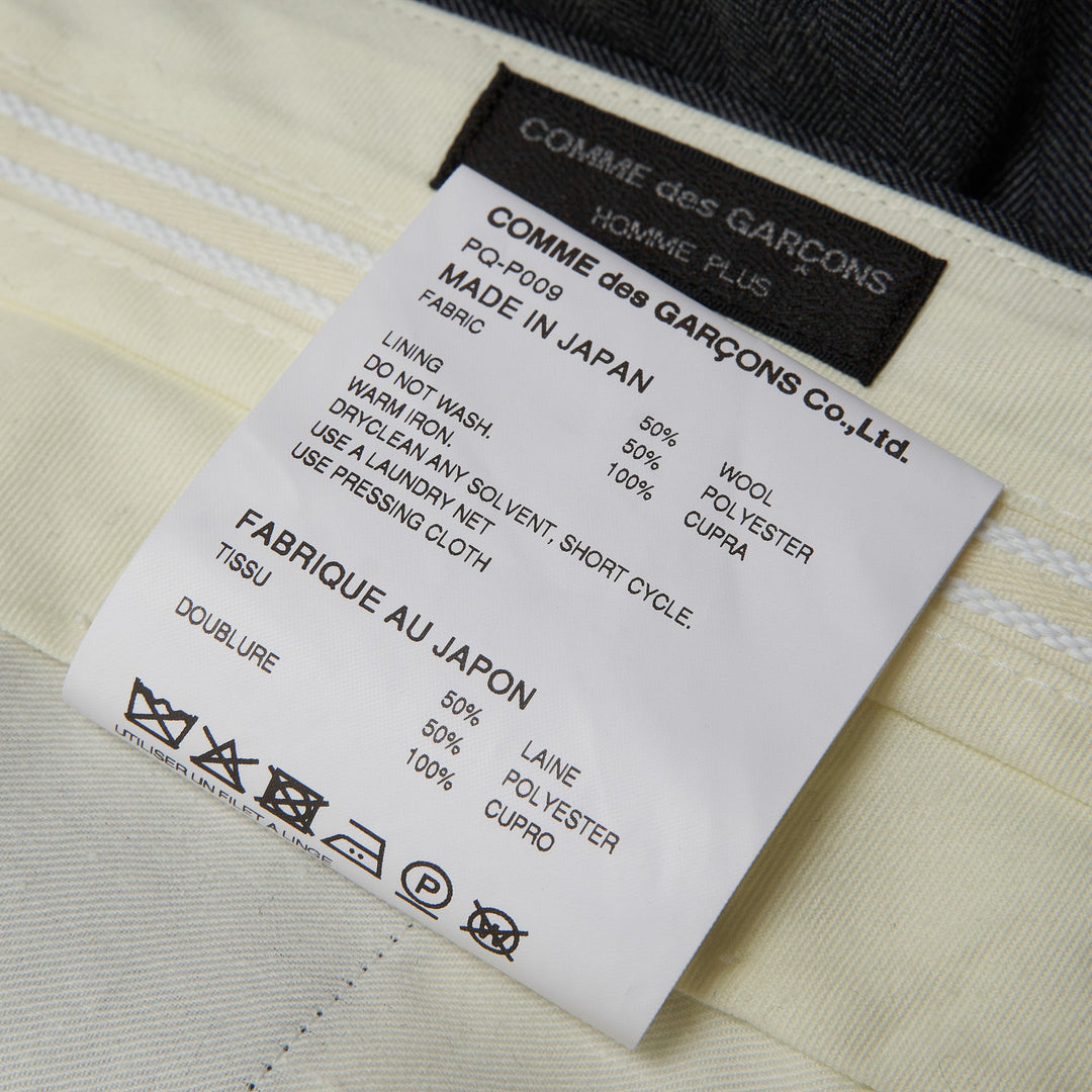 COMME des GARCONS HOMME PLUS Pleated Wide-Leg Shorts in charcoal grey with deep forward pleats and high-rise waistband, front view on white background