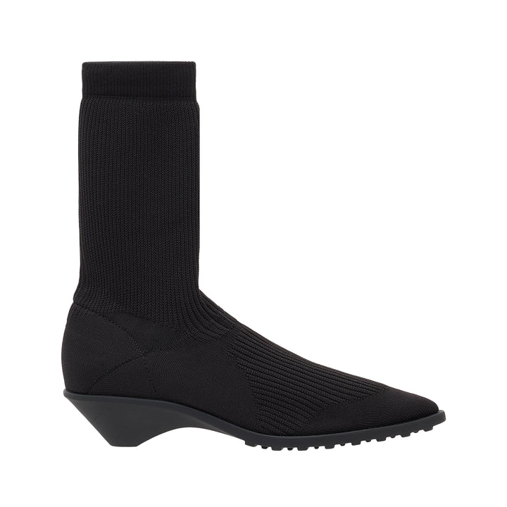 Issey Miyake black fine-gauge ribbed knit sock boot with a pointed toe, star-motif panel at the vamp, and sculptural moulded wedge sole, shown in profile against a white background