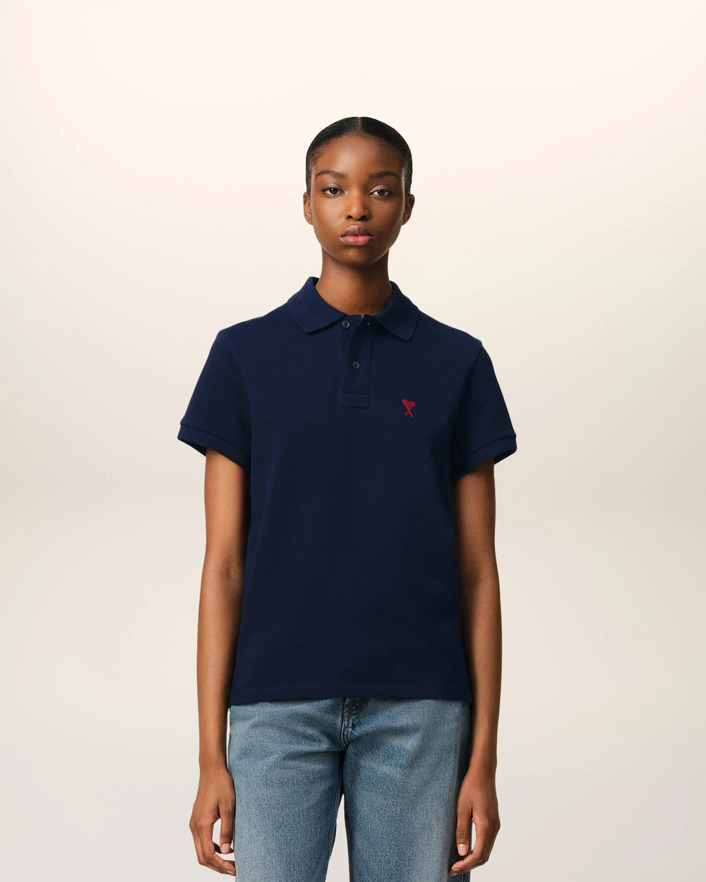 AMI De Coeur black piqué polo shirt with embroidered red heart logo at the chest, laid flat on white background