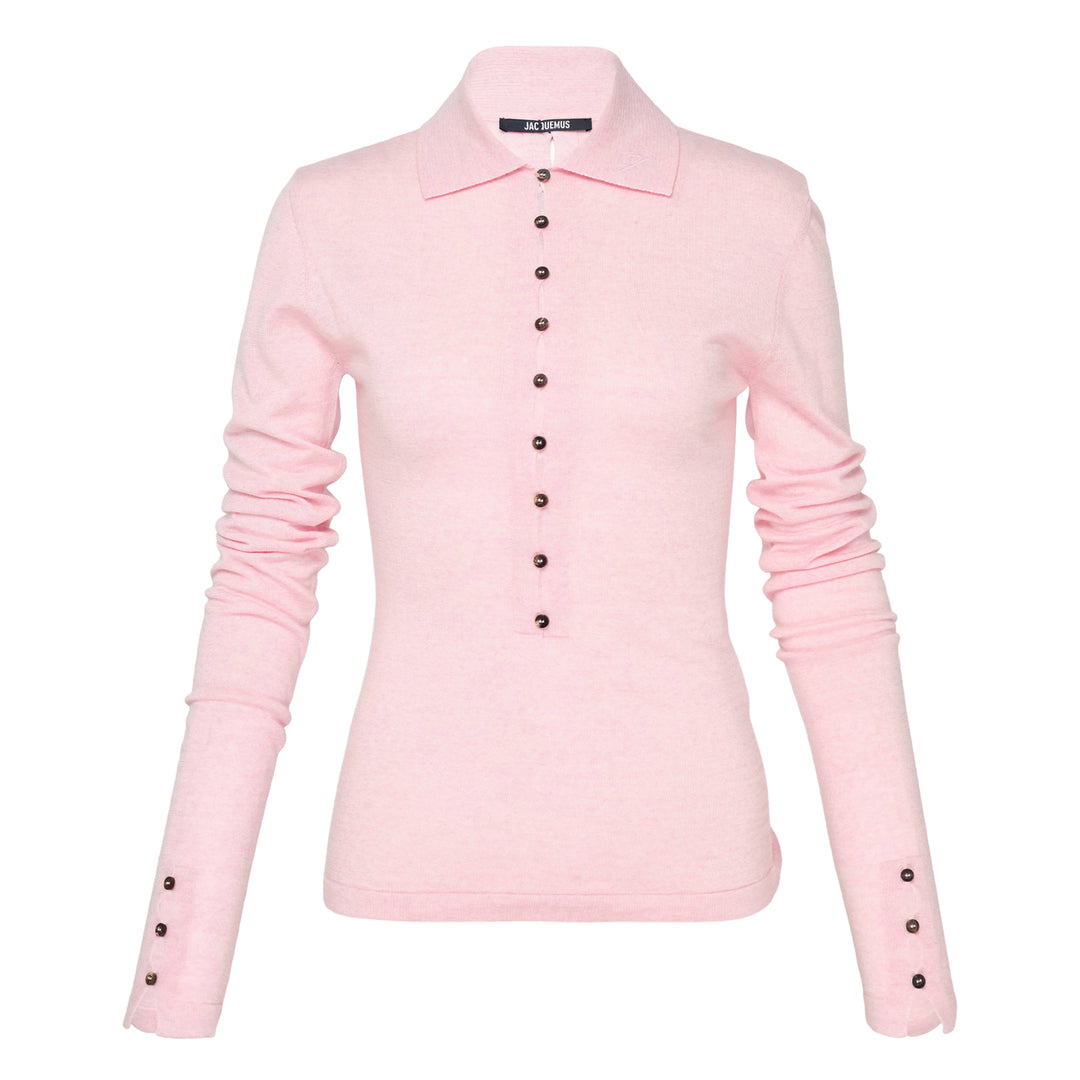 Jacquemus Le Polo Merino long-sleeve knit polo in blush pink with dark snap-button placket, ruched sleeves, and snap-button cuffs, displayed on a flat lay against a white background