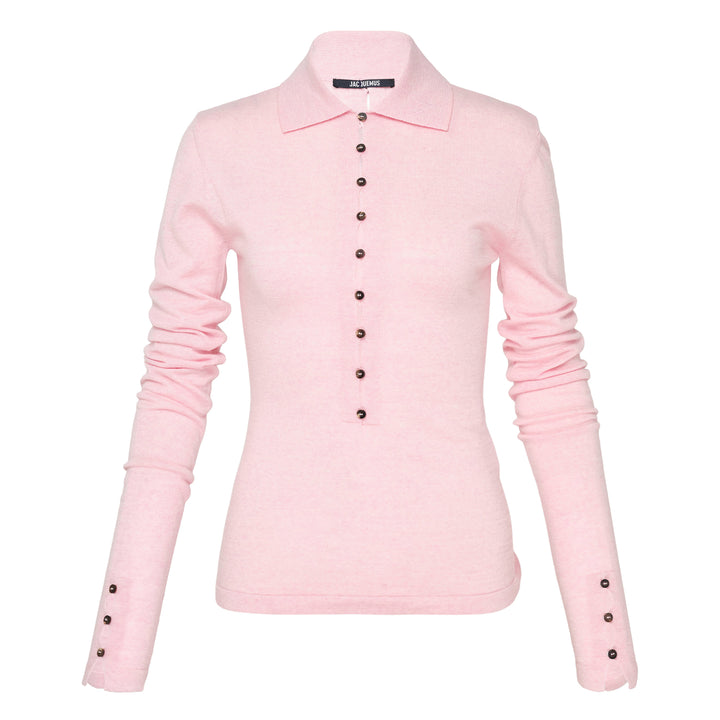 Jacquemus Le Polo Merino long-sleeve knit polo in blush pink with dark snap-button placket, ruched sleeves, and snap-button cuffs, displayed on a flat lay against a white background
