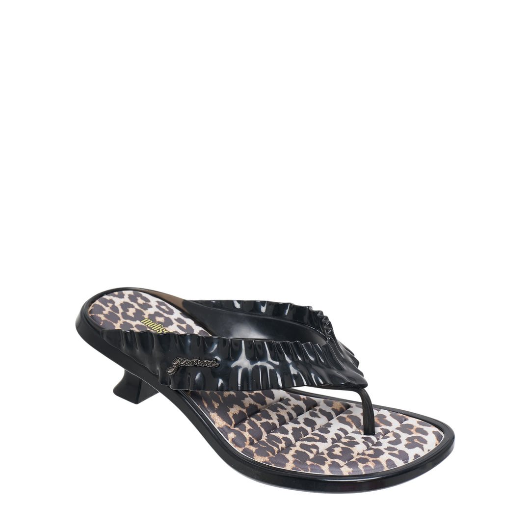 Ganni x Melissa black thong kitten heel sandal with ruched petal-texture strap, gold script logo hardware, leopard-print footbed, and sculptural low heel, shown in profile