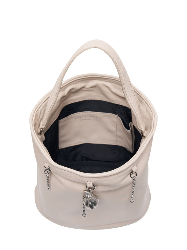 Marge Sherwood Wired Bucket Bag in pebbled cream leather with a single top handle, three silver chain drops, and a sculptural metal charm pendant at centre - view 3