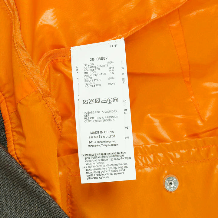 sacai Nylon Twill Bomber Blouson in olive green, featuring dual zip closure, contrast amber yellow hem lining, angled chest pockets, and ribbed knit trims, displayed flat on a white background - view 3