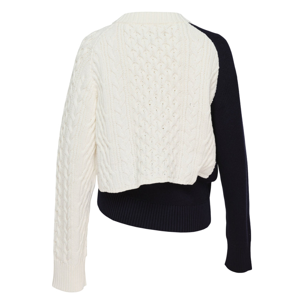 sacai Cotton Cashmere Knit Pullover with chunky cable-knit cream body, contrasting smooth navy sleeve panel, asymmetric ribbed hem, and crew neckline