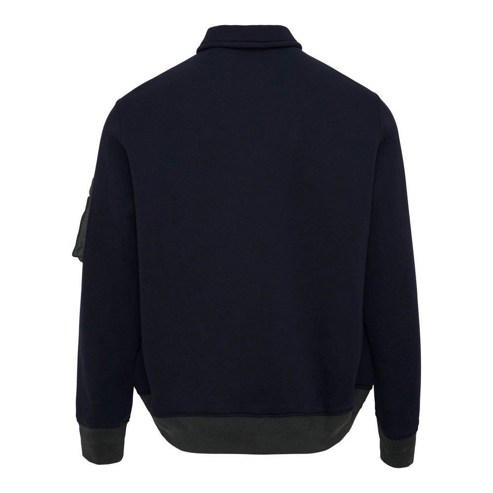 sacai Sponge Sweat Half-Zip Polo in navy, featuring a spread collar, silver half-zip, sleeve utility pocket, and contrast nylon bomber hem band