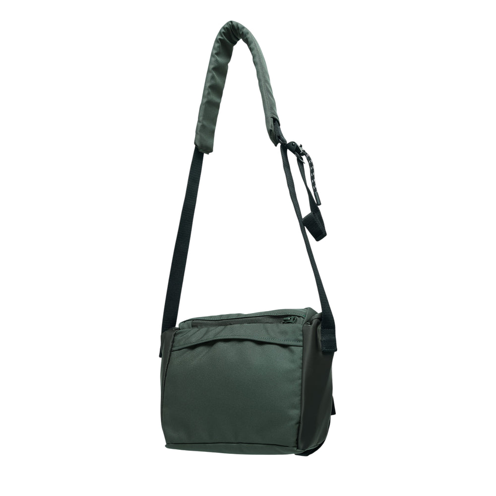 sacai Utility Shoulder Bag in olive nylon, featuring a padded wrapped adjustable strap, quick-release clip hardware, dual front pockets with zip and snap-button closures, and matte black buckle detailing on the body