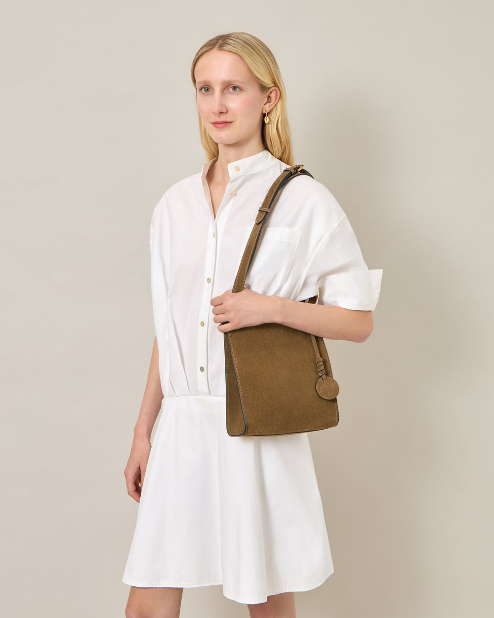 Mulberry Mini Soft Suede Tote in warm taupe suede, displayed upright showing tonal saddle stitching, knotted leather tie closure, adjustable crossbody strap, and embossed Mulberry tree medallion charm
