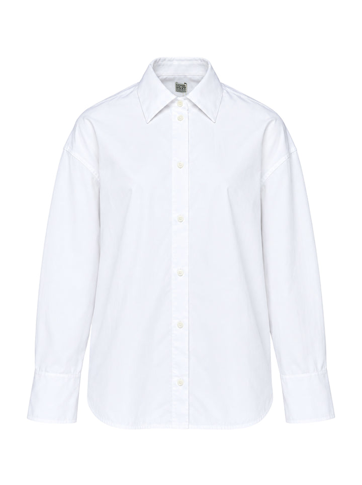Totême Boxy Poplin Shirt in white, featuring a pointed collar with woven monogram label, full button fastening, long sleeves with barrel cuffs, and a relaxed oversized silhouette