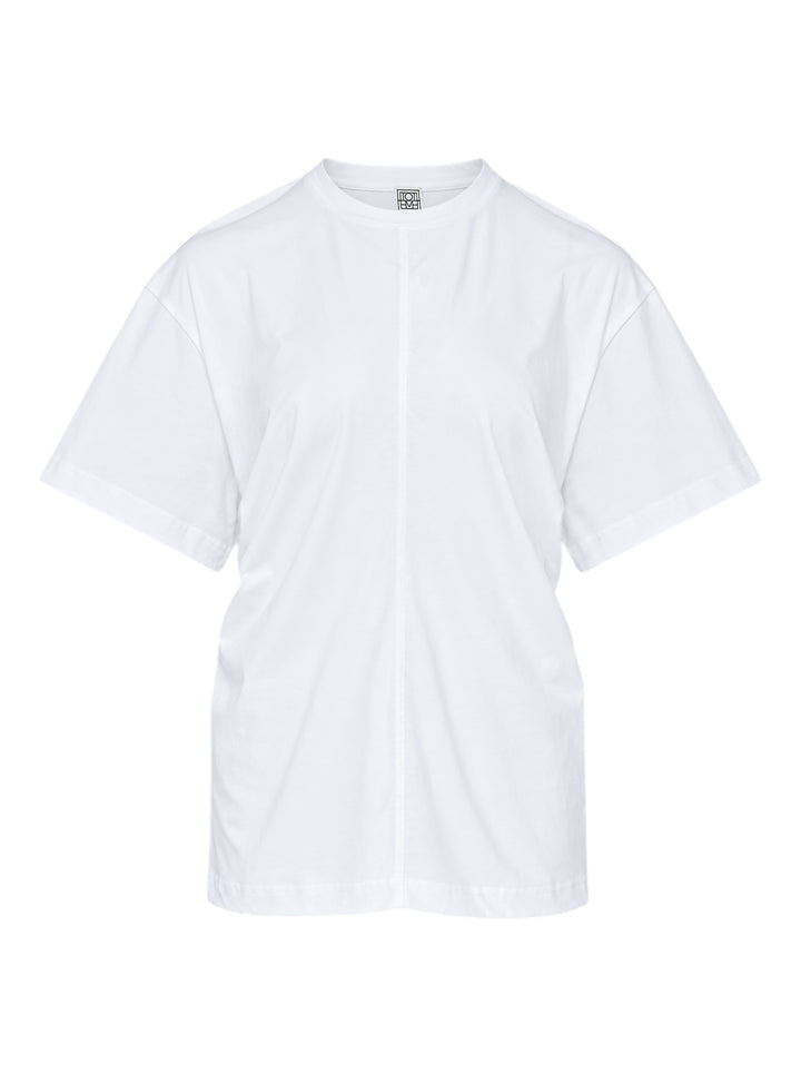 Totême Slouch Waist Jersey Top in white, featuring an oversized dropped-shoulder silhouette, centre-front seam, crew neckline, and short sleeves with folded cuffs, photographed flat on a white background