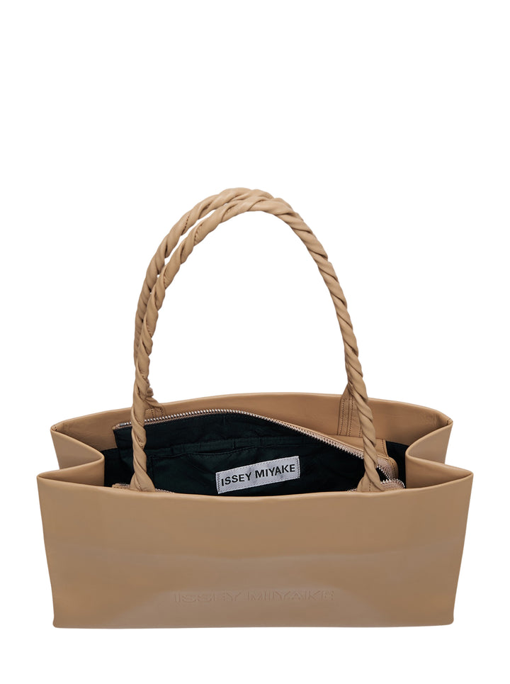 Issey Miyake tan leather Paper Bag handbag with sculptural rope-twisted single shoulder handle and embossed logo on the front panel, photographed front-facing against a white background - view 3