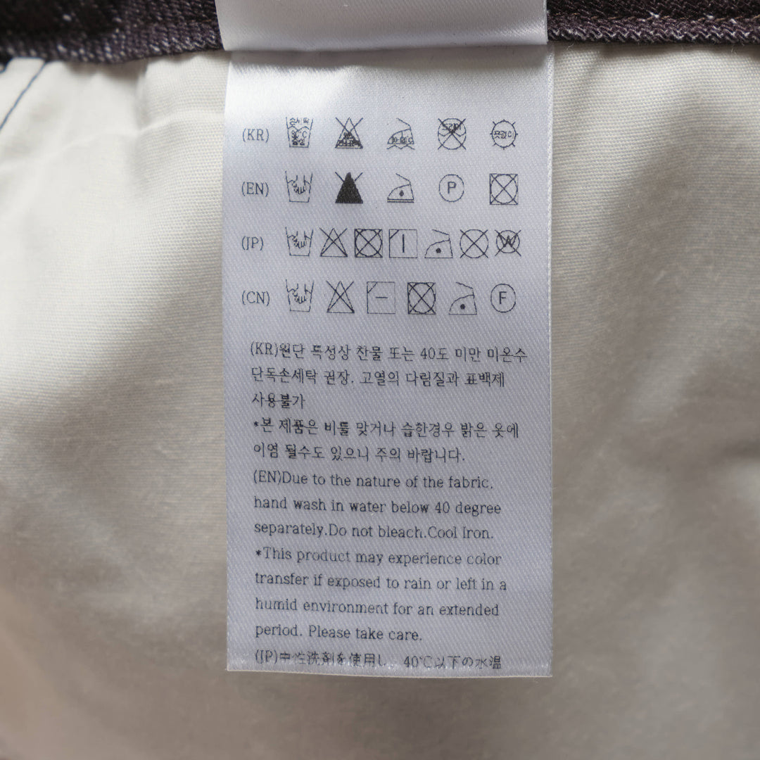 Andersson Bell Illusion Patchwork Denim Skirt with trompe l'œil patchwork print, high waist, silver-tone button closure, and pleated underlay hem on a white background