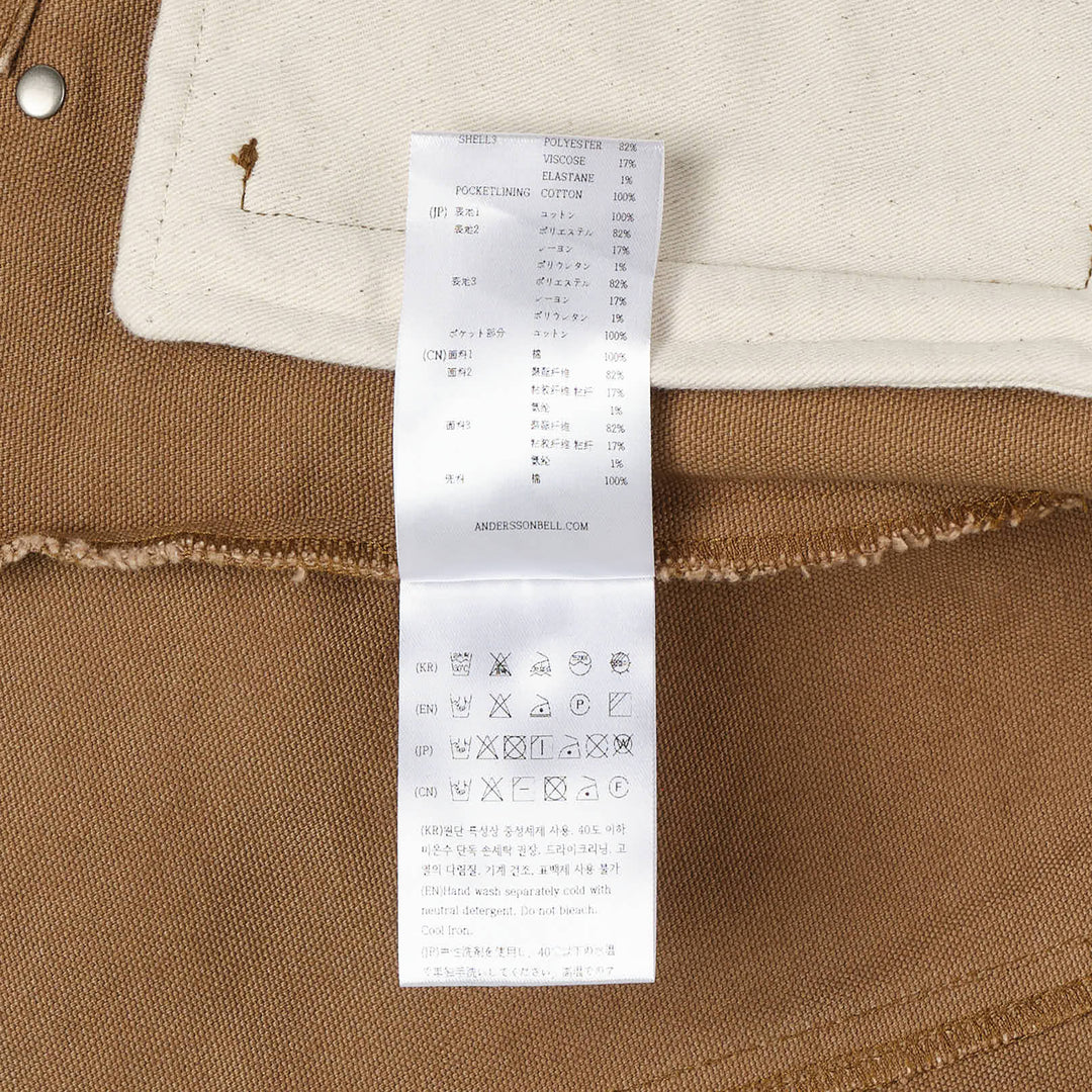 Andersson Bell Layered Studded Vest Shirt — cropped khaki denim vest with silver dome studs and frayed edges over a long-sleeve brown tartan plaid shirt, snap-button front closure and ADSB logo patch