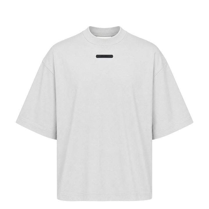 Fear of God Essentials Merch Tee in washed charcoal, featuring a boxy oversized silhouette, dropped shoulders, tonal chest branding patch, and a mock-neck collar