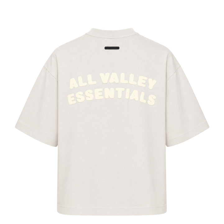 Fear of God Essentials Merch Graphic Tee in blue-grey with tonal Greek-letter chest print, displayed flat on a white background
