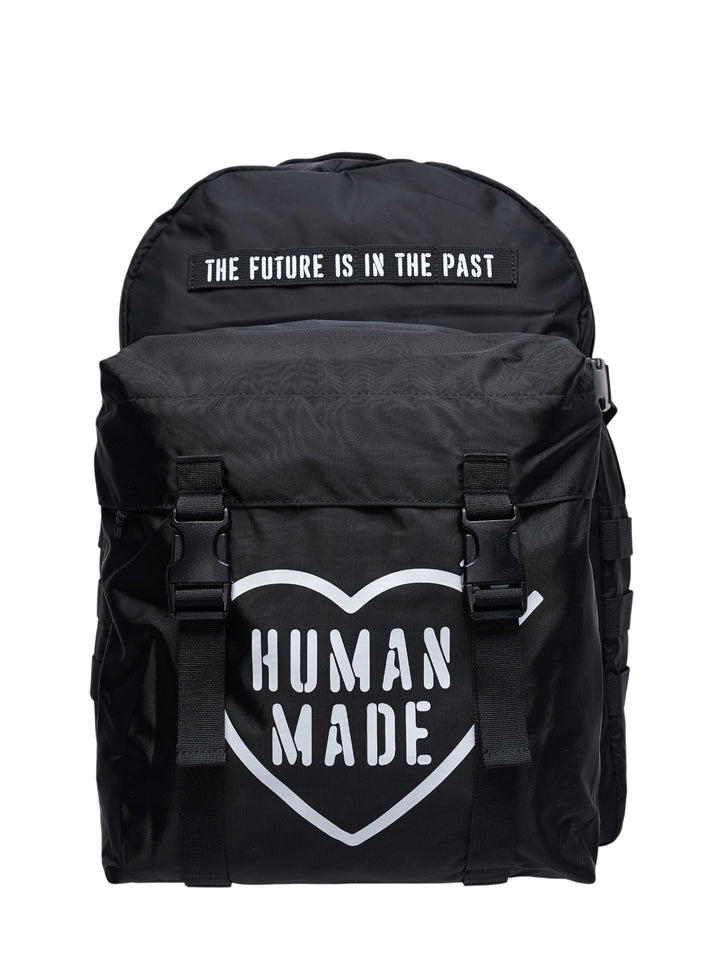 Human Made Military Backpack in black nylon featuring the heart logo print, twin buckle-clip strap fastenings on the front pocket, and an embroidered 'The Future Is In The Past' patch