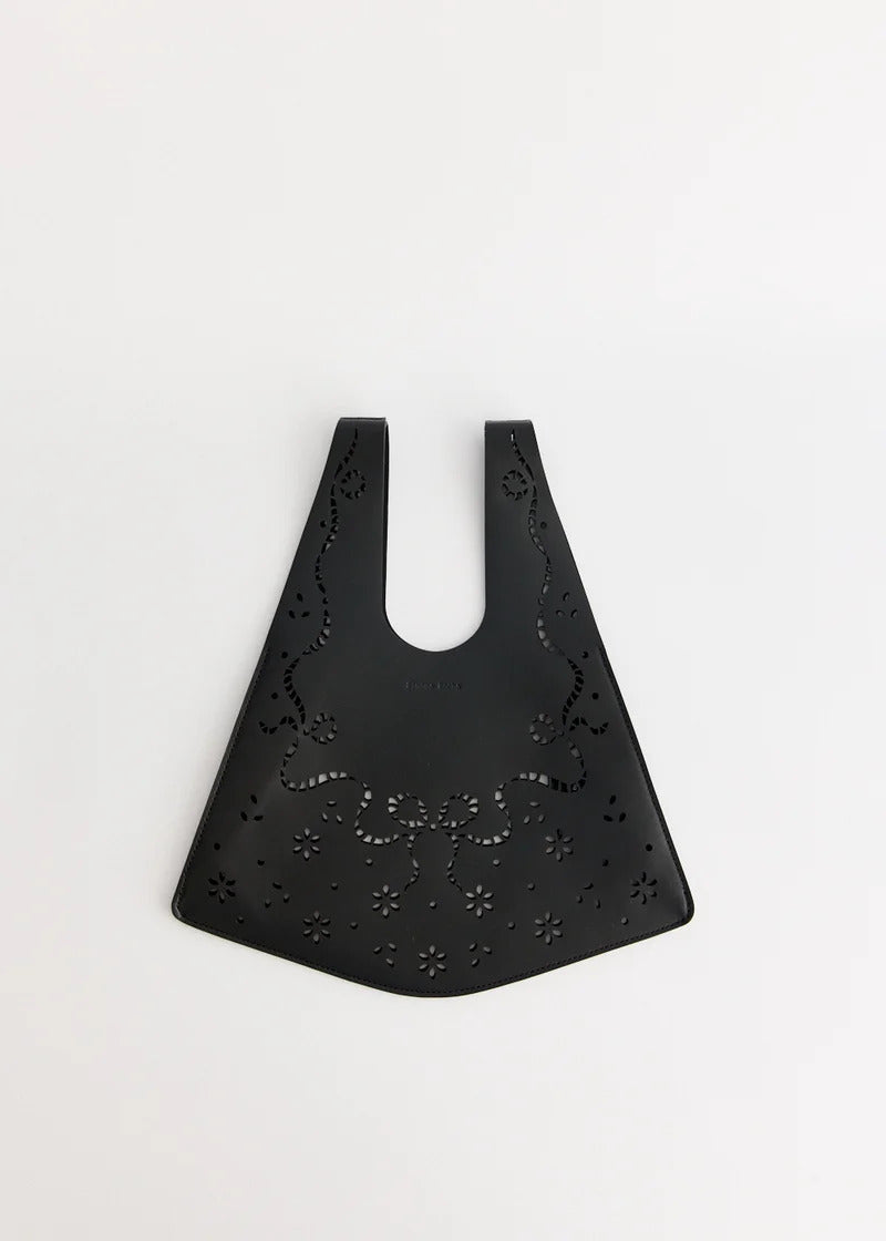 Simone Rocha mini shopper bag in black leather with lasercut lace-inspired bow and floral cutouts, shown flat against a white background