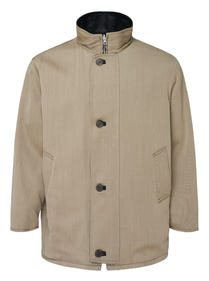 Auralee reversible wool twisted twill coat in beige with stand collar, button front and black leather reverse visible at the collar