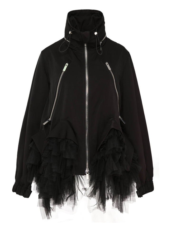 Noir Kei Ninomiya black oversized long sleeve jacket with high drawstring neck, silver zip closures, angled chest zip pockets, and layered black tulle ruffle hem, displayed flat on a white background