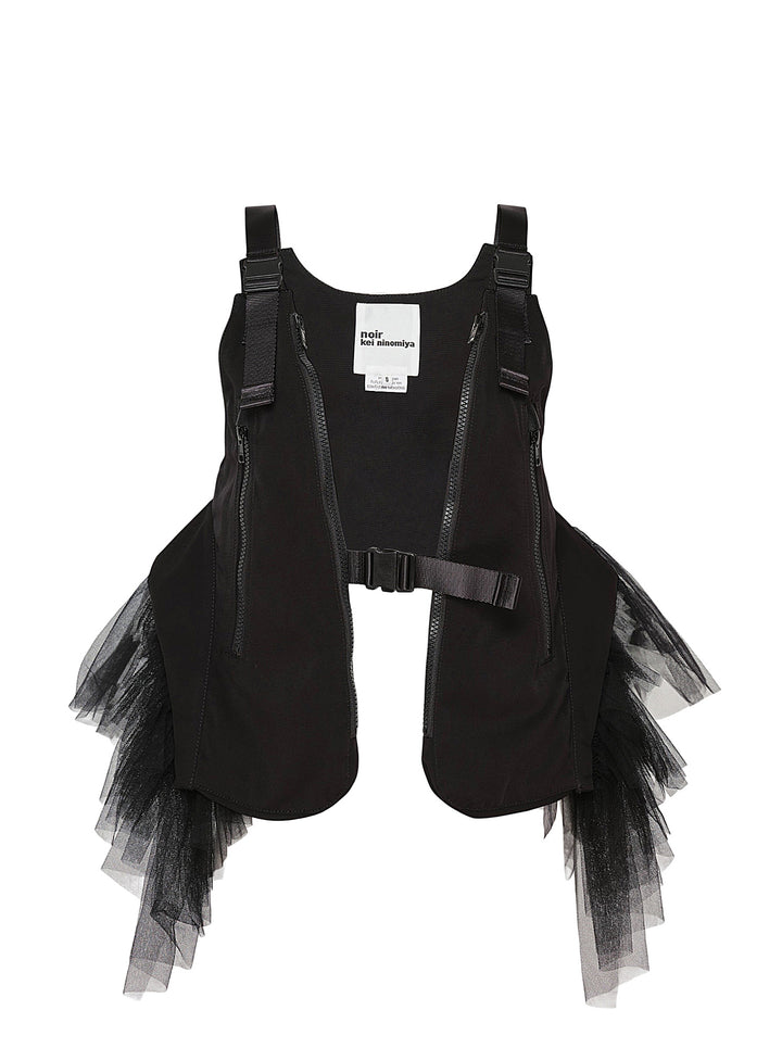 Noir Kei Ninomiya black harness vest with diagonal zip pockets, clip-buckle webbing straps, and cascading sheer tulle panels at the sides, photographed flat on a white background