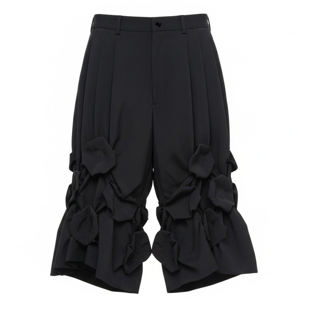 Comme des Garçons Homme Plus black wool tropical shorts with knotted fabric floral clusters and voluminous ruffled hem, front view on white background