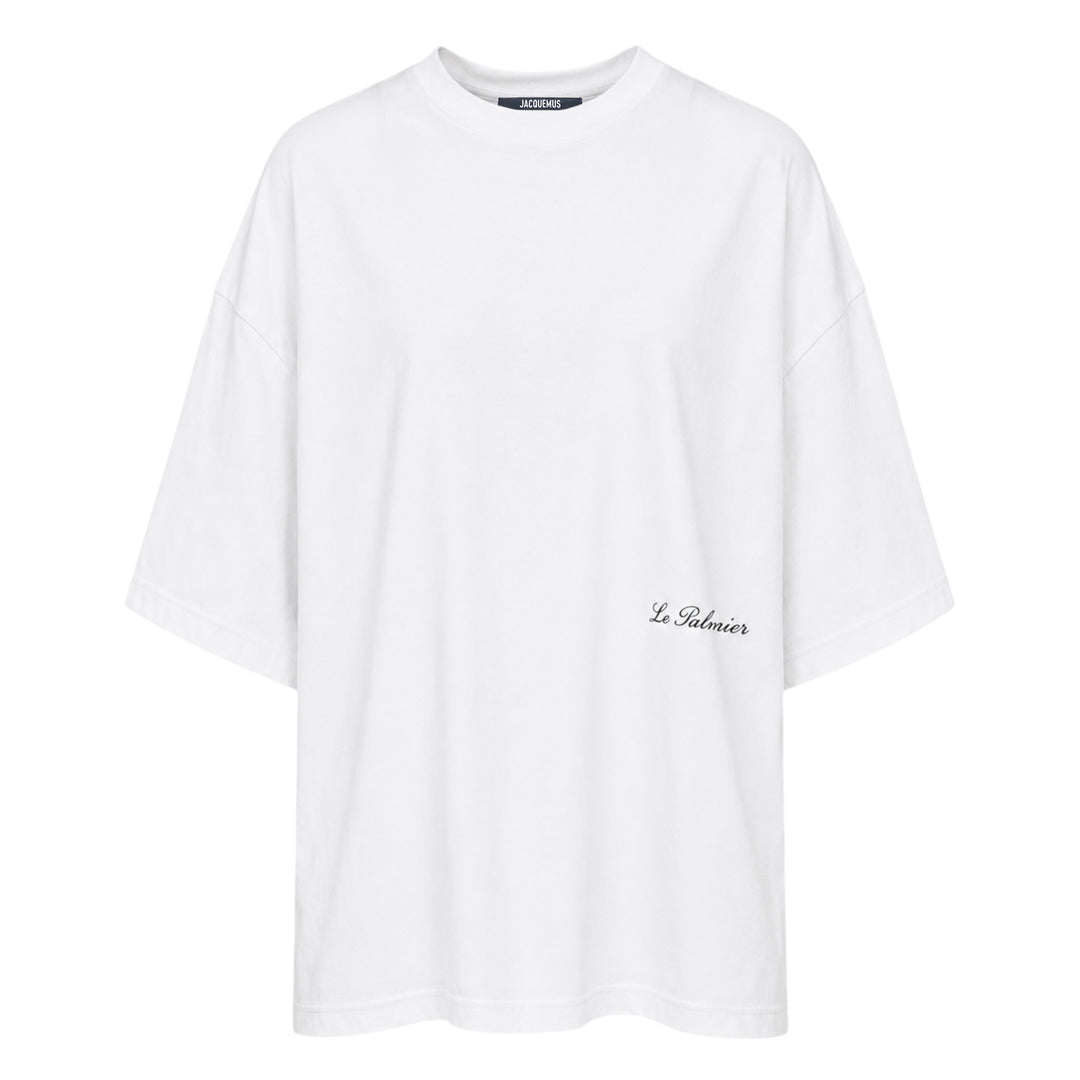 Jacquemus Le Palmier oversized white cotton tee with drop shoulders and 'Le Palmier' script embroidery at the hem, product flat lay