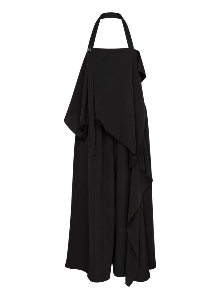 Y's black halter apron jumpsuit with an asymmetric draped bib and wide-leg silhouette, shown from the front