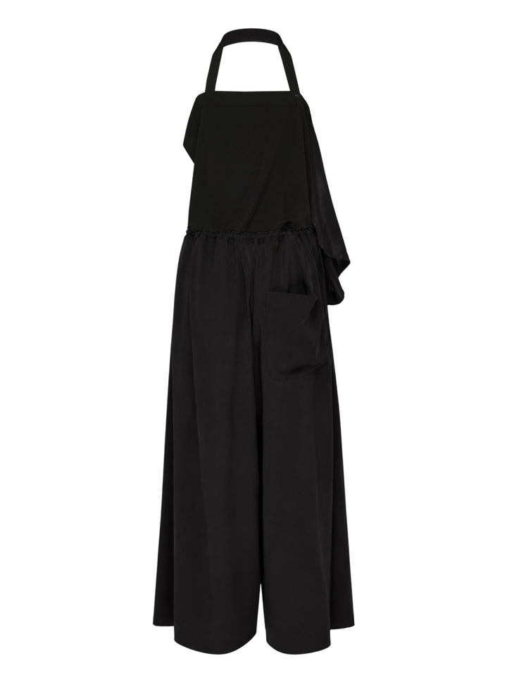 Y's black halter apron jumpsuit with an asymmetric draped bib and wide-leg silhouette, shown from the front - view 2