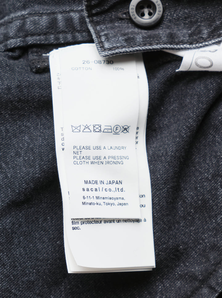 sacai oversized black washed denim shirt dress with dual chest patch pockets, mixed button hardware, full-length button front, and longline curved hem — flat lay on white background - view 3