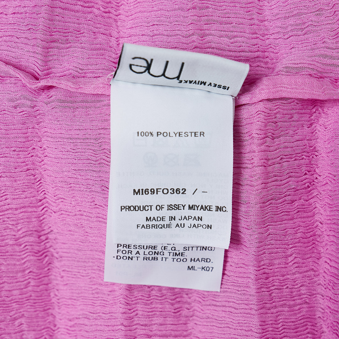 me Issey Miyake Accordion See-Through Crepe Cardigan in pink, featuring horizontal accordion pleating, ruffled lettuce-edge trim, dark contrast button-through front, and a relaxed long-sleeve silhouette