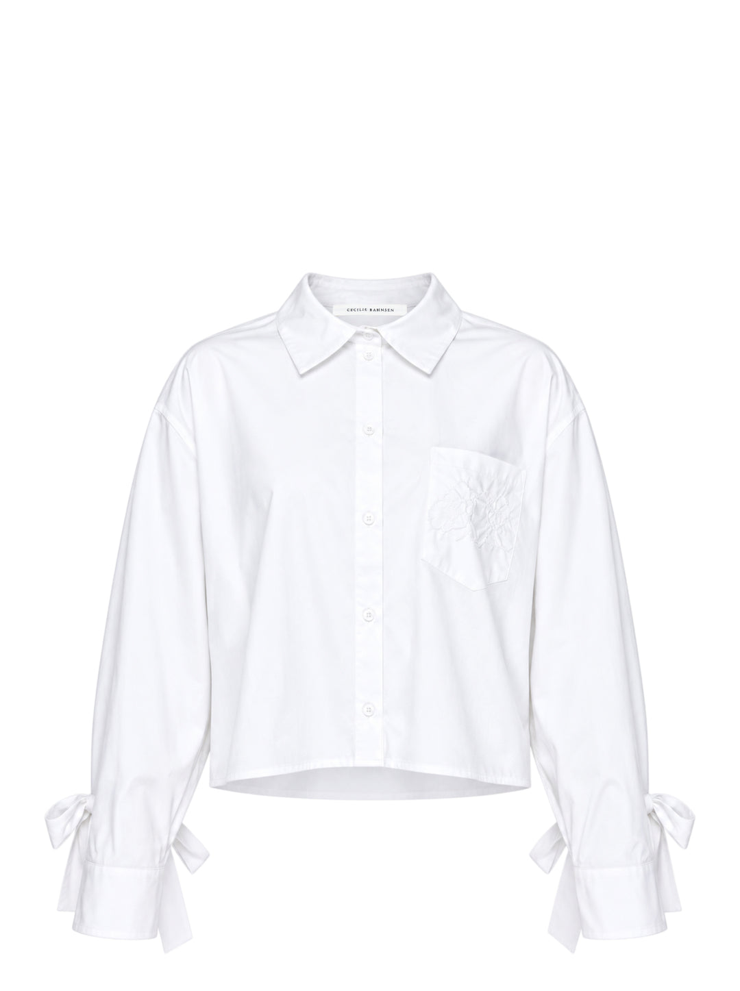 Cecilie Bahnsen Frina cropped white cotton shirt with bow-tied flared cuffs, tonal floral embroidered chest pocket, and button-through front placket, displayed flat on a white background