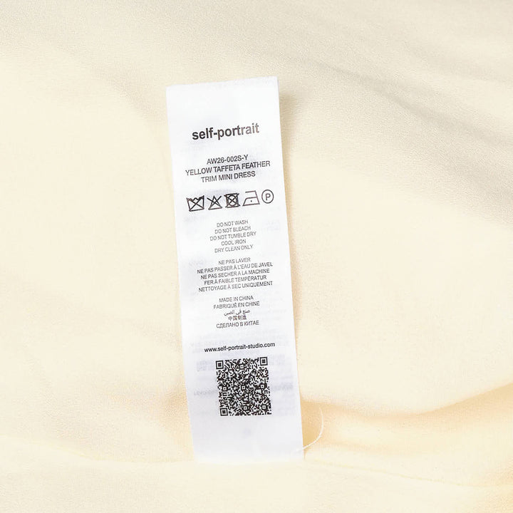 Self-Portrait pale yellow taffeta halter mini dress with feather and floral appliqué trim along the hem, displayed flat on a white background