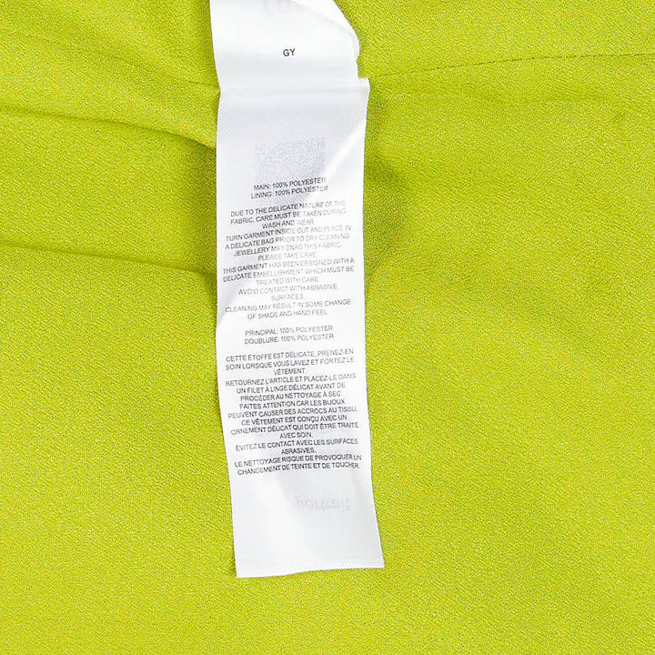 Self-Portrait lime green satin halter mini dress with structured bow waist detail, styled with matching slim-cut coordinating trousers, flat lay on white background