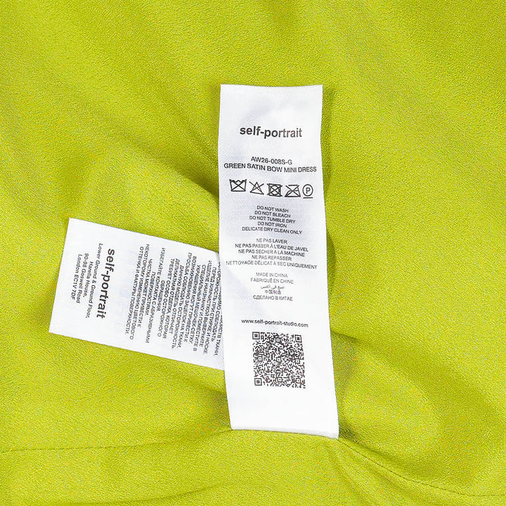 Self-Portrait lime green satin halter mini dress with structured bow waist detail, styled with matching slim-cut coordinating trousers, flat lay on white background