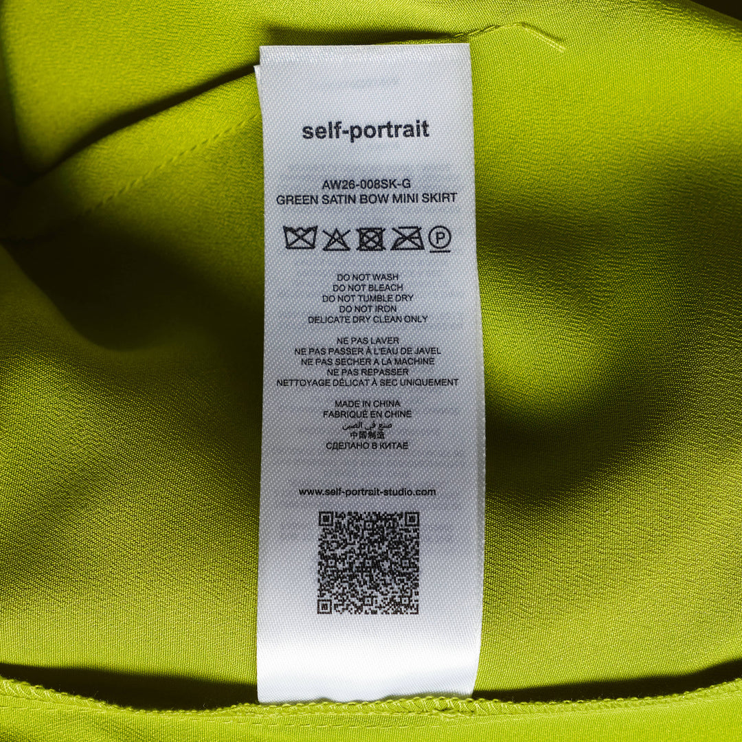 Self-Portrait lime green belted mini skirt over straight-leg trousers hybrid garment, laid flat on a white background, featuring a self-covered buckle belt and smooth satin-finish fabric