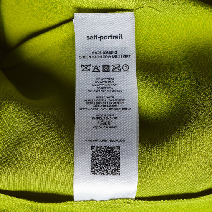 Self-Portrait lime green belted mini skirt over straight-leg trousers hybrid garment, laid flat on a white background, featuring a self-covered buckle belt and smooth satin-finish fabric