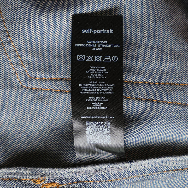 Self-Portrait Indigo Wide Leg Jeans in dark indigo denim with contrast amber topstitching, patch pockets, turned cuffs, and a tan leather belt with gold-tone buckle, laid flat on a white background