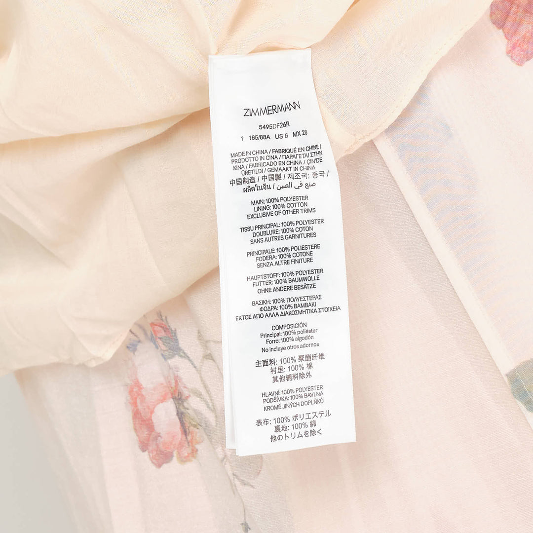 Zimmermann Pleated Tiered Midi Dress in blush floral print, featuring spaghetti straps, a pleated fitted bodice with bow detail, and four cascading ruffle tiers falling to a midi length