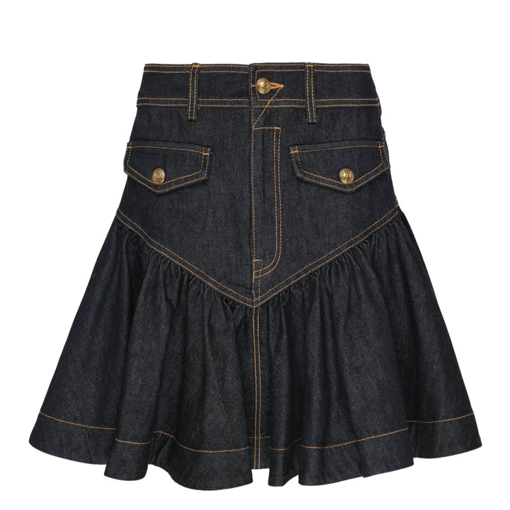 Zimmermann Denim Frill Mini Skirt in dark indigo with orange contrast topstitching, chevron seam detail, front patch pockets with branded gold snap buttons, and a gathered ruffle hem