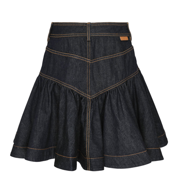 Zimmermann Denim Frill Mini Skirt in dark indigo with orange contrast topstitching, chevron seam detail, front patch pockets with branded gold snap buttons, and a gathered ruffle hem