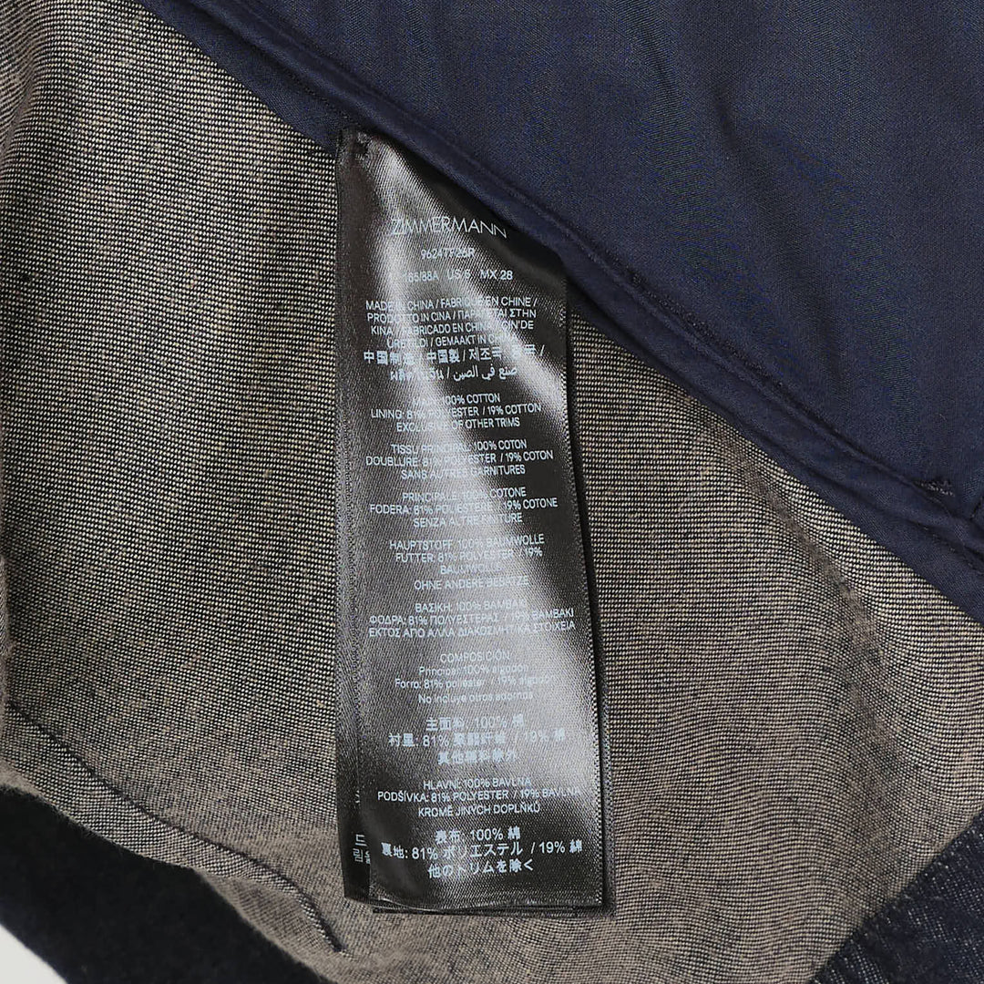 Zimmermann Draped Denim Jacket in dark indigo with cascading chest overlay, voluminous balloon sleeves, and gold-tone centre-front zip, shown on a plain white background