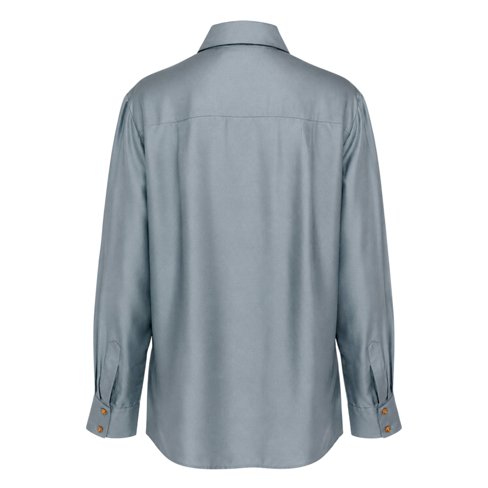 Zimmermann tassel tie neck blouse in slate blue with self-tie bow, fringe tassel ends, amber buttons, and wide barrel cuffs, displayed flat on a white background