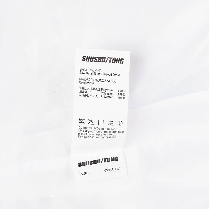 SHUSHU/TONG ivory textured short sleeve drop-waist dress with self-fabric bow detail at the waist and pleated skirt, front view