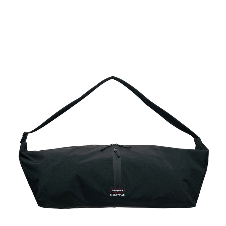 Fear of God ESSENTIALS x Eastpak Shell Bag Large in black, front view showing oversized body, wide shoulder strap, central zip closure, and co-branded woven label