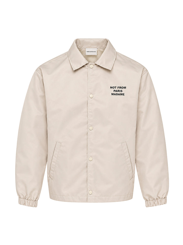Drôle de Monsieur Not From Paris Madame slogan coach jacket in ecru with snap-button closure, point collar, elasticated cuffs, and embroidered chest slogan