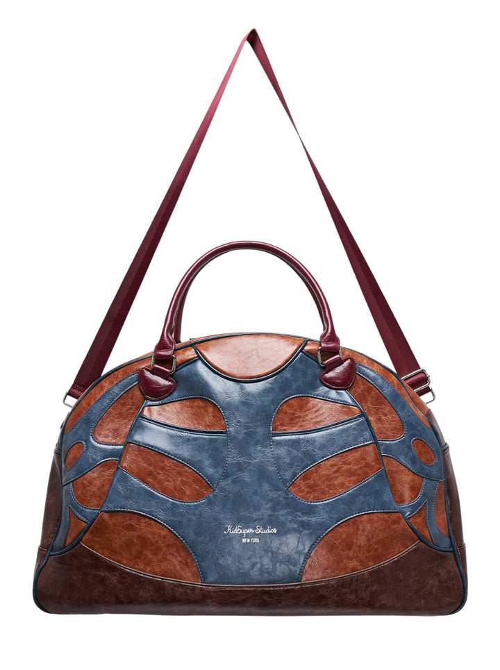 KidSuper Studios bowling bag in blue and tan patchwork faux leather with burgundy top handle and shoulder strap
