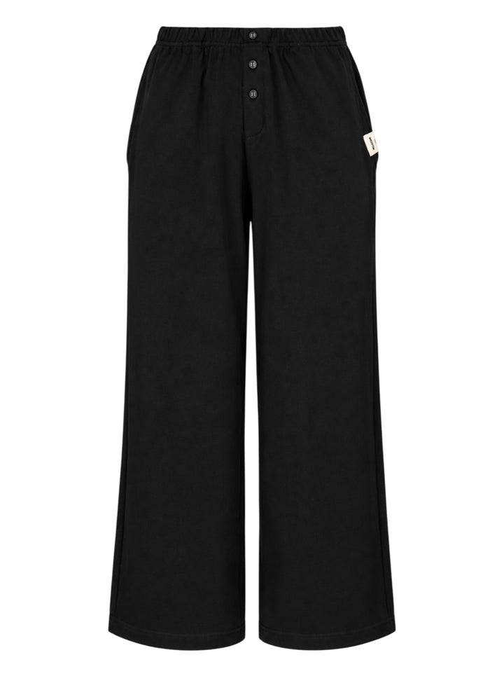 Glowny Button Fly Wide Leg Pants in black, featuring an elasticated waistband, three-button fly placket, wide-leg silhouette, and woven brand label tab at the hip