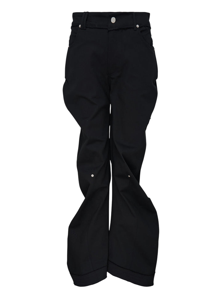Nache Rawcut Curved Pants in black, featuring a sculpted bowed leg, raw-cut waistband, metal button closure and rivet details, shown from the front