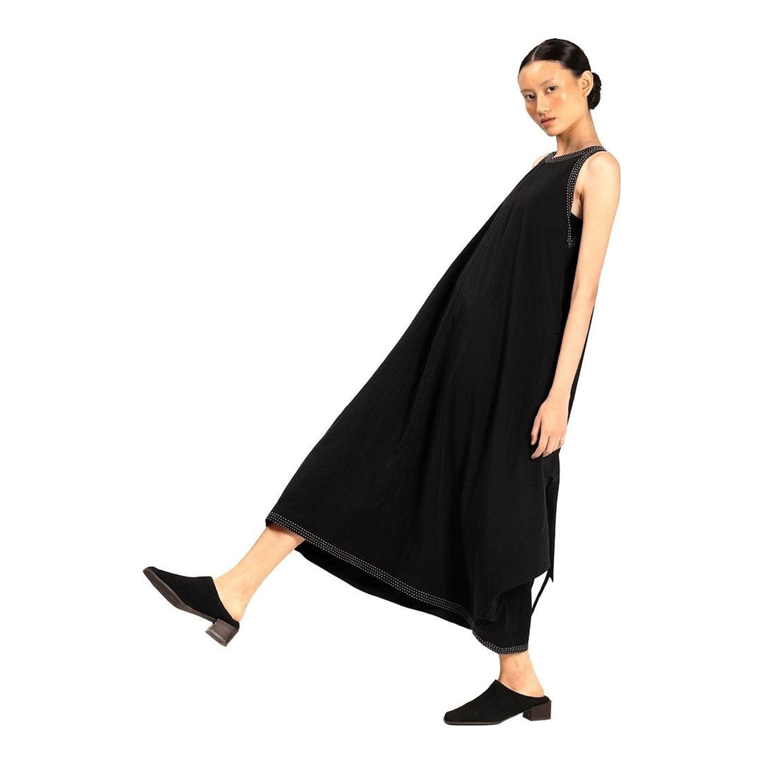 Model wearing an Anaabu black sleeveless midi dress with a voluminous A-line silhouette, asymmetric handkerchief hemline, and fine metallic stud trim at the neckline and hem - packshot